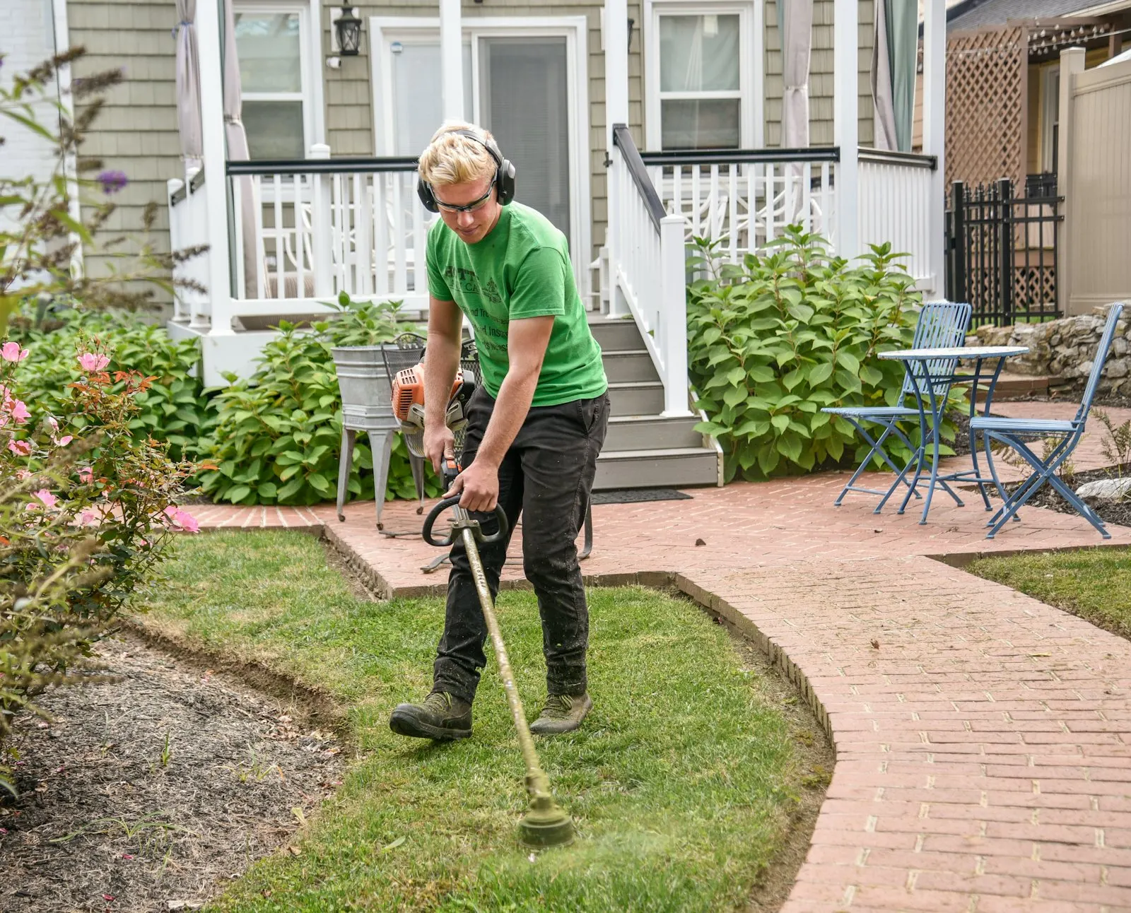 String trimmer running along a sidewalk edge cleaning up the grass line.